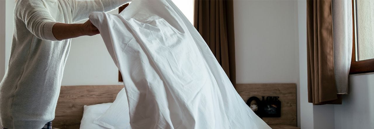 woman making the bed holding a flat sheet