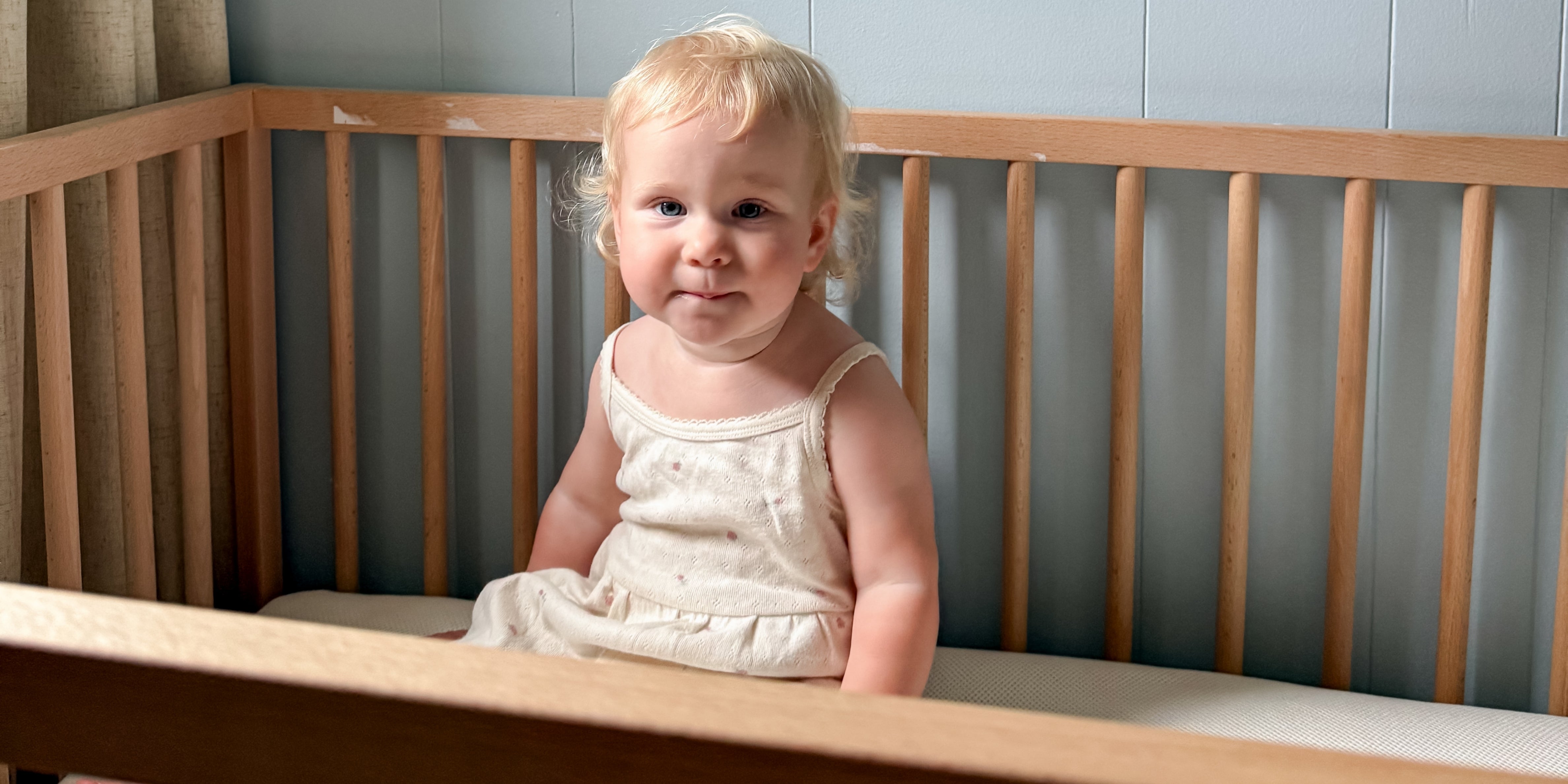 Toddler sitting on 2-stage crib mattress in crib