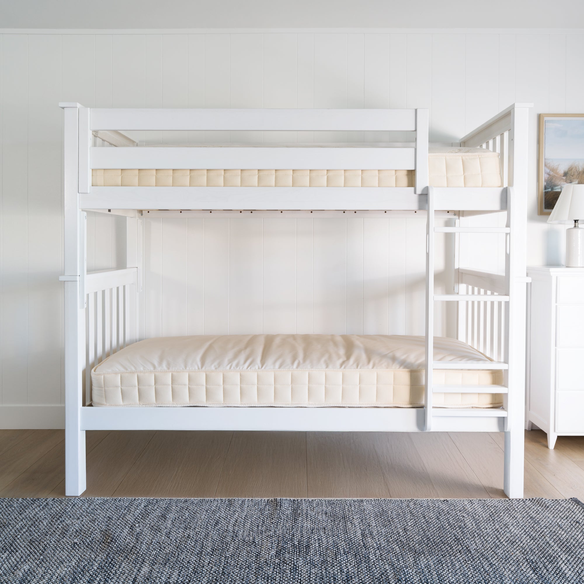White wooden bunk bed with bare mattresses in a bright, minimalist bedroom setting. #color_washed white #size_Twin/Twin Bunk