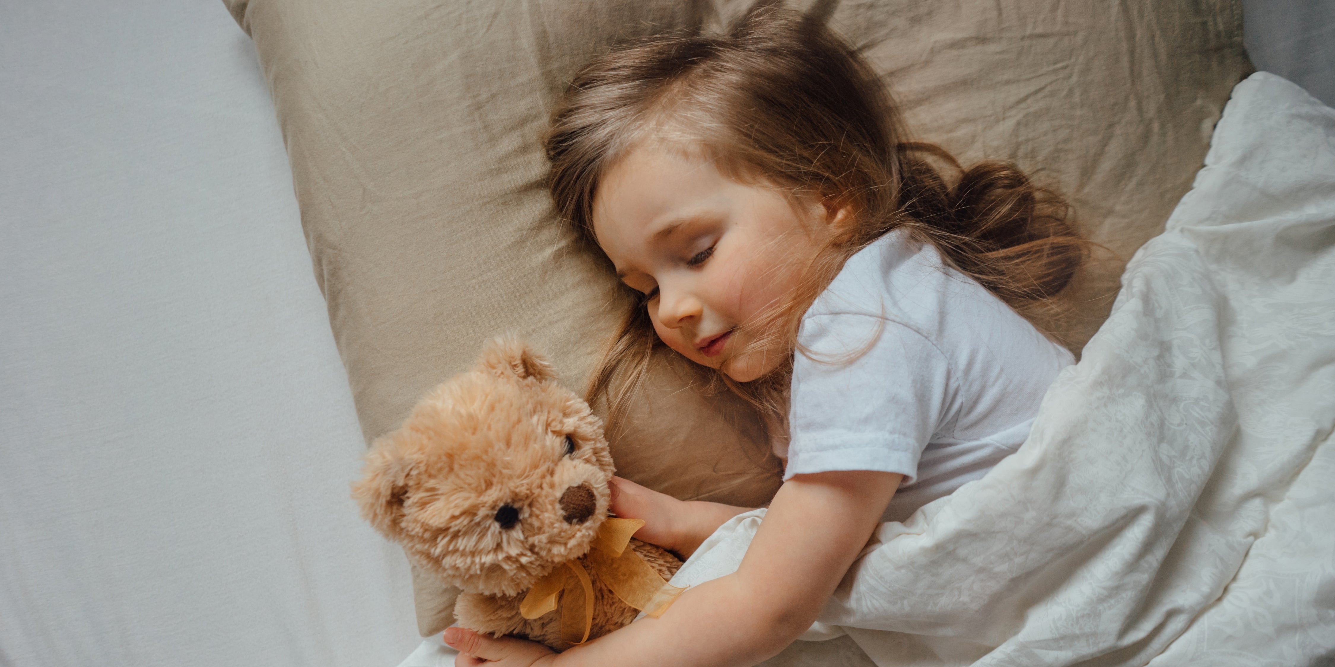 Toddler napping in bed with teddy bear