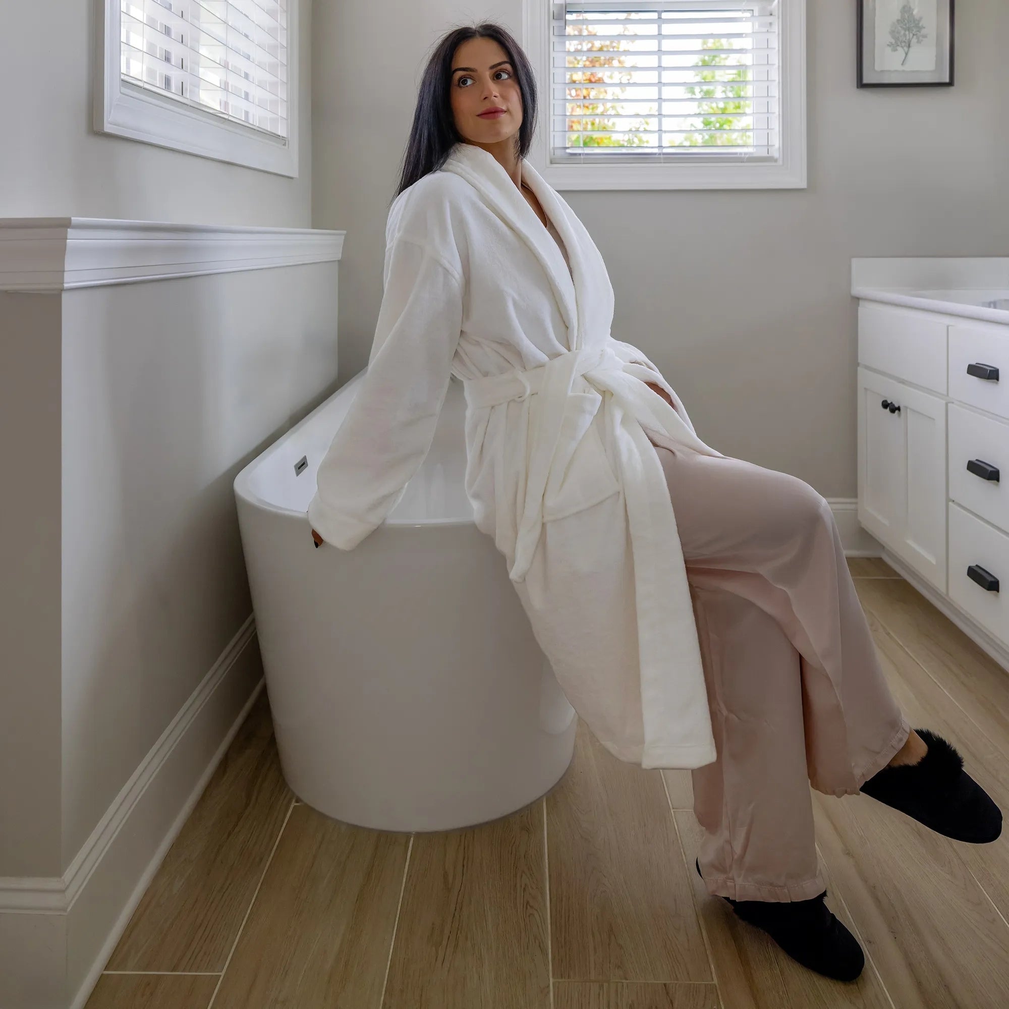 Woman in a white robe sitting on a white bathtub in a bathroom. #color_arctic snow