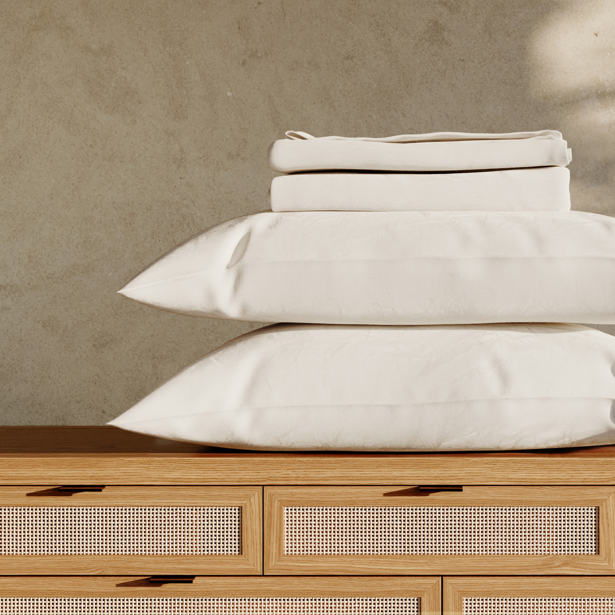 Stack of white pillows and folded sheets on a wooden dresser with a neutral background #color_arctic snow