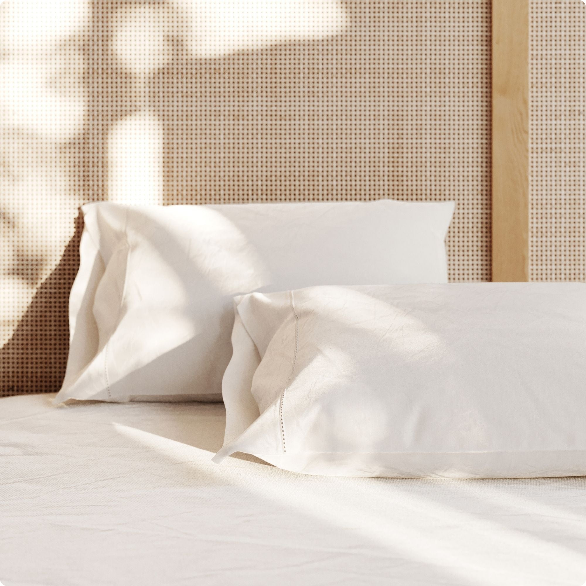 Two white pillows on a bed with a woven headboard.