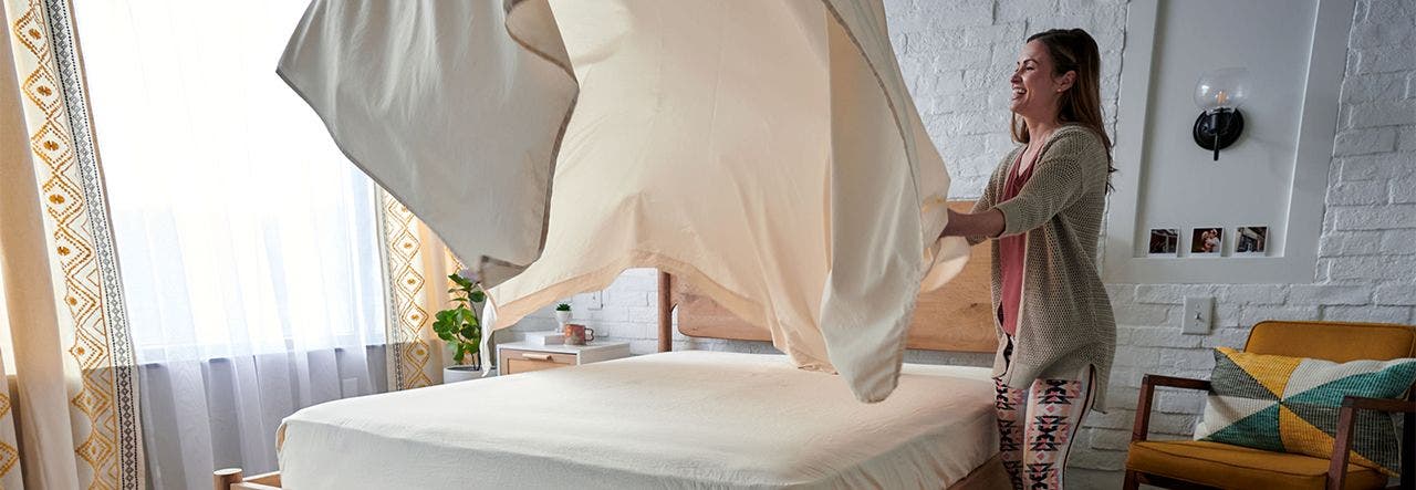 Woman shaking out a bedsheet to make her bed