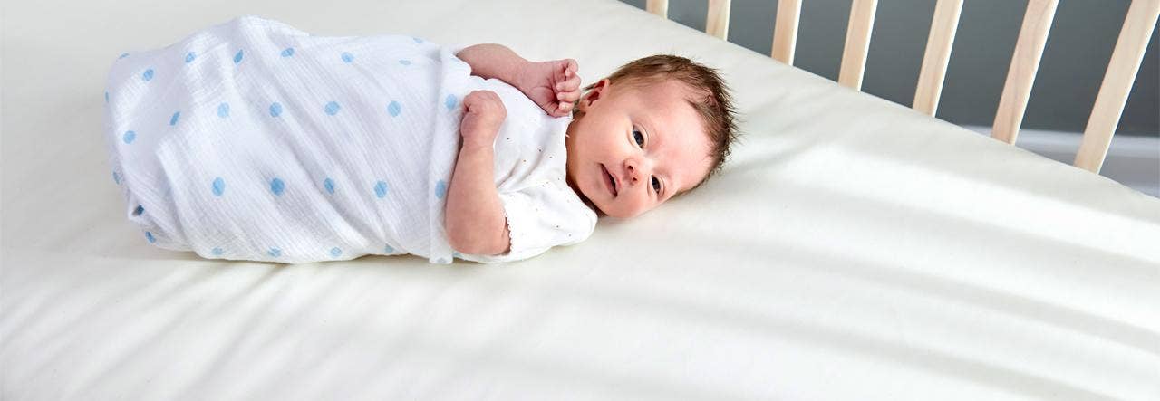 Swaddled baby lying on bare crib mattress surface