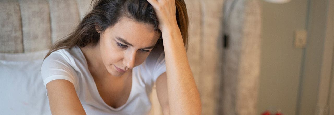 Woman sitting up in bed with her head in her hands, suffering from anxiety