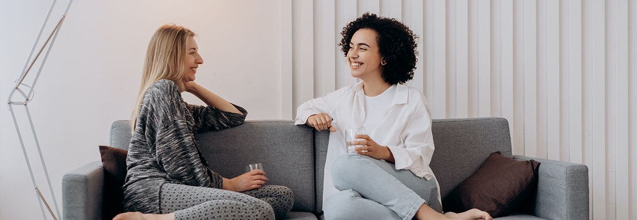 Two young women sitting on a couch and chatting happily