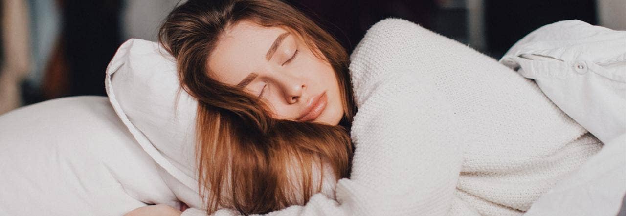 Woman in a white sweater sleeping on a white pillow