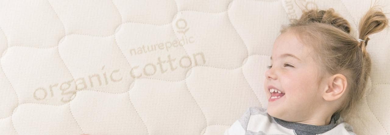 Smiling little girl on a Naturepedic certified organic mattress