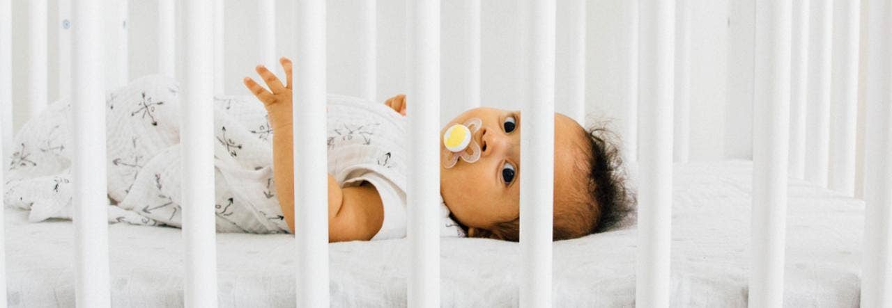 Baby with pacifier lying on back and looking through the crib slats