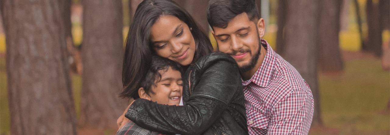 Mother hugging her young young outdoors, father leans into her shoulder