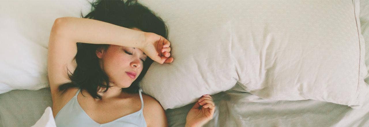 Woman in light tank top trying to sleep cooler at night