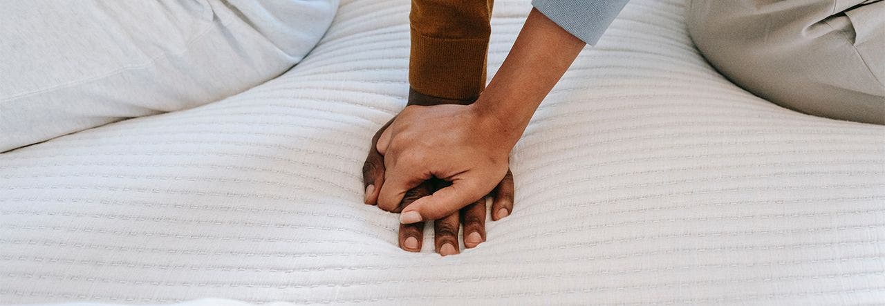 Man and woman sitting on their bed and holding hands