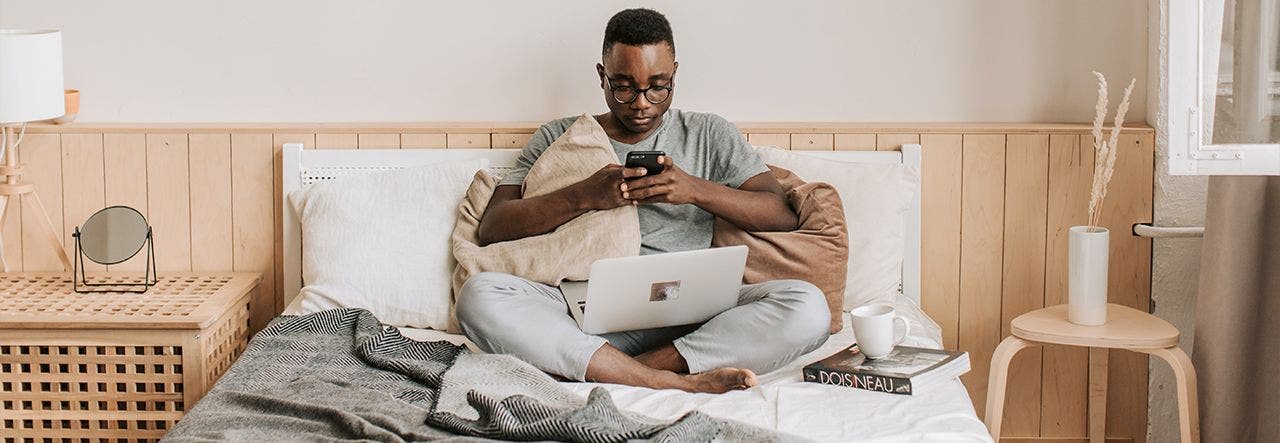 Young man sitting up in bed and researching when to replace a mattress