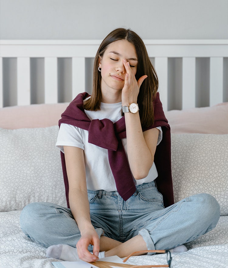 Woman sitting corss-legged on her bed and rubbing her eyes