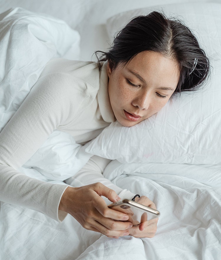 Woman propped up in bed and snoozing her alarm