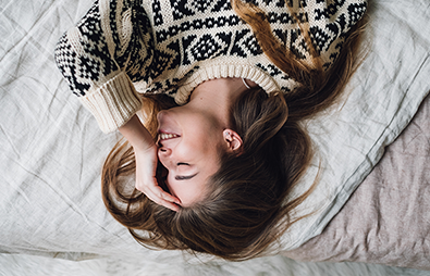 woman laying in bed smiling with hand on forehead