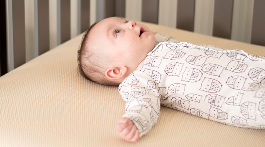 Awake baby lying on a breathable organic crib mattress 