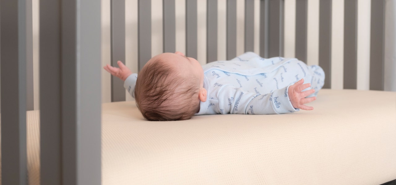 Side view of a baby lying awake on a crib mattress