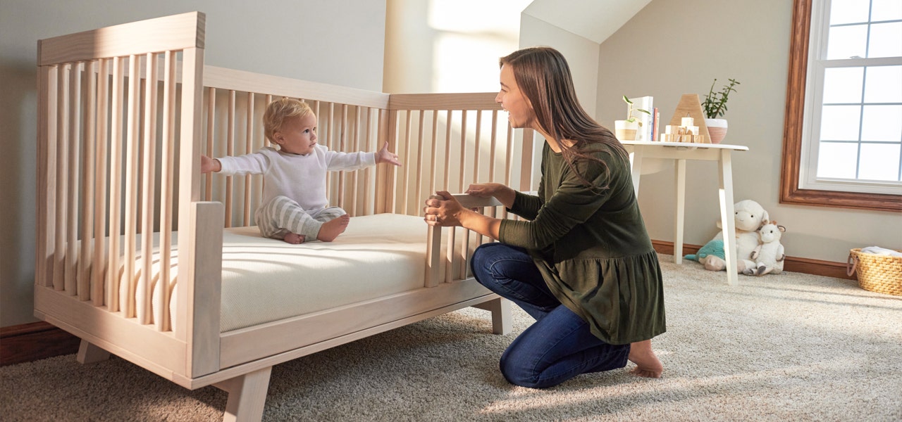 Woman kneelingn next to crib and smiling at her baby