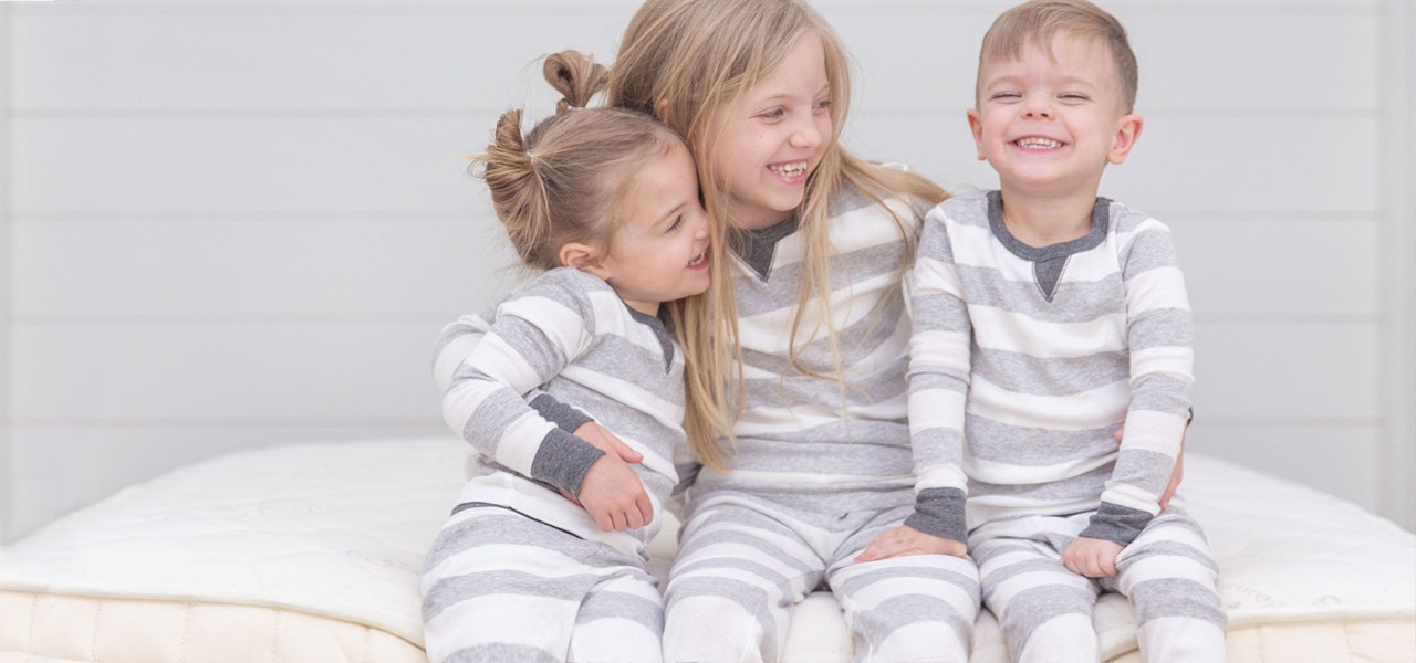 Three children in matching striped pajamas sitting on a Naturepedic mattress