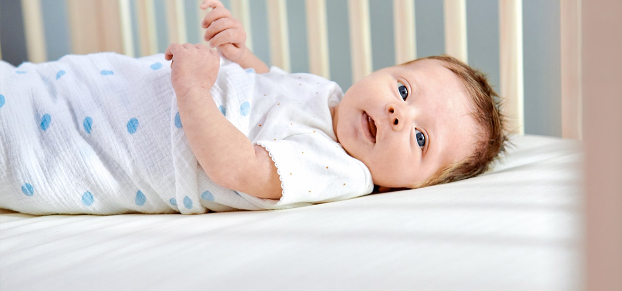 Side view of swaddled baby, lying awake on a Naturepedic crib mattress