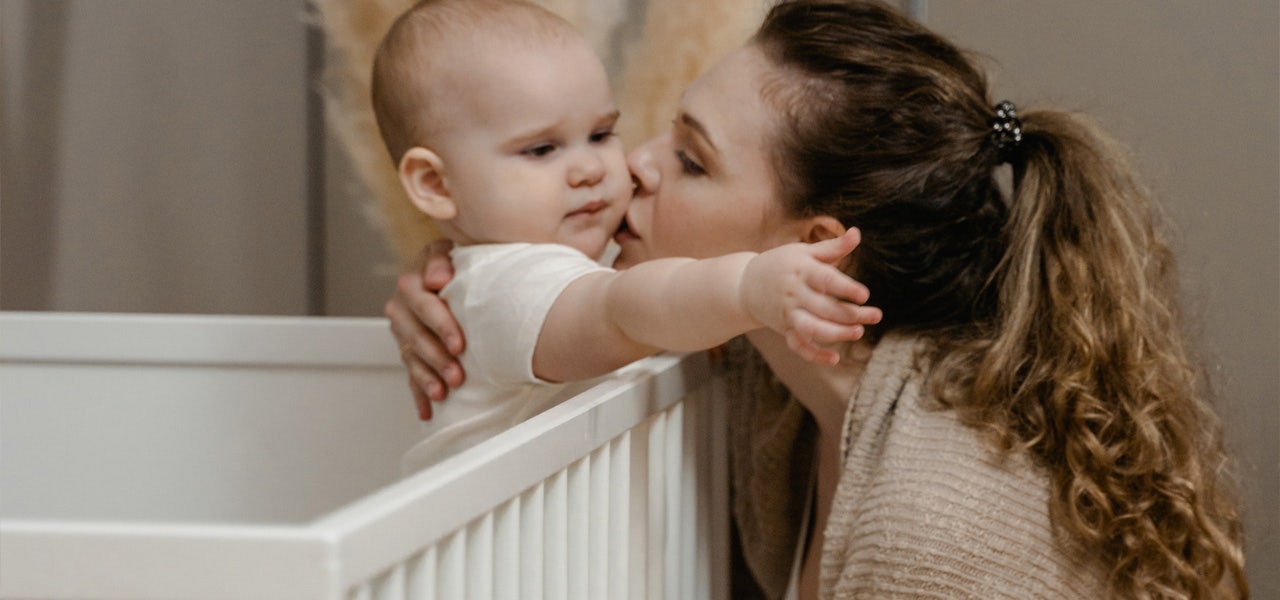 Mother kissing her baby who stands inside the crib