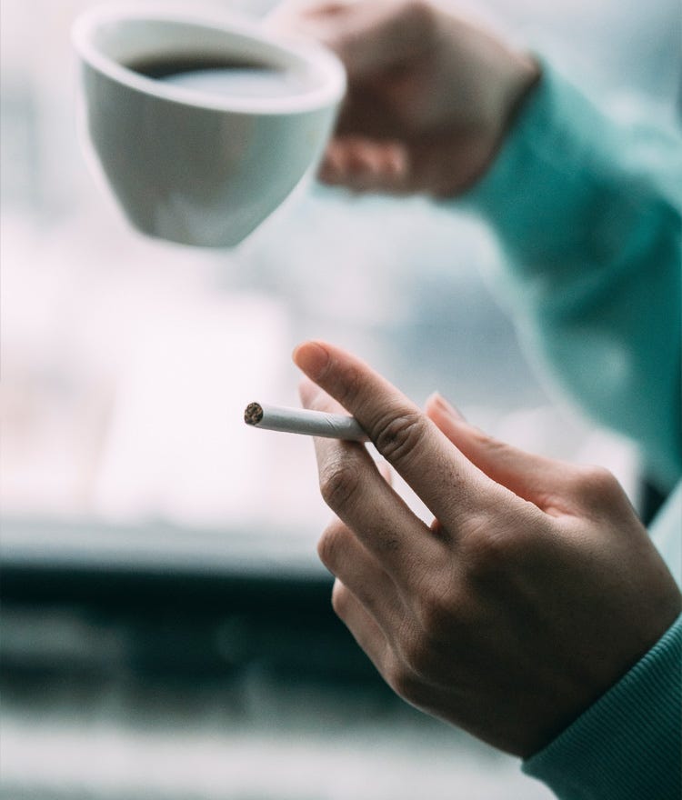 Woman's hands holding a cigarette and a cup of coffee