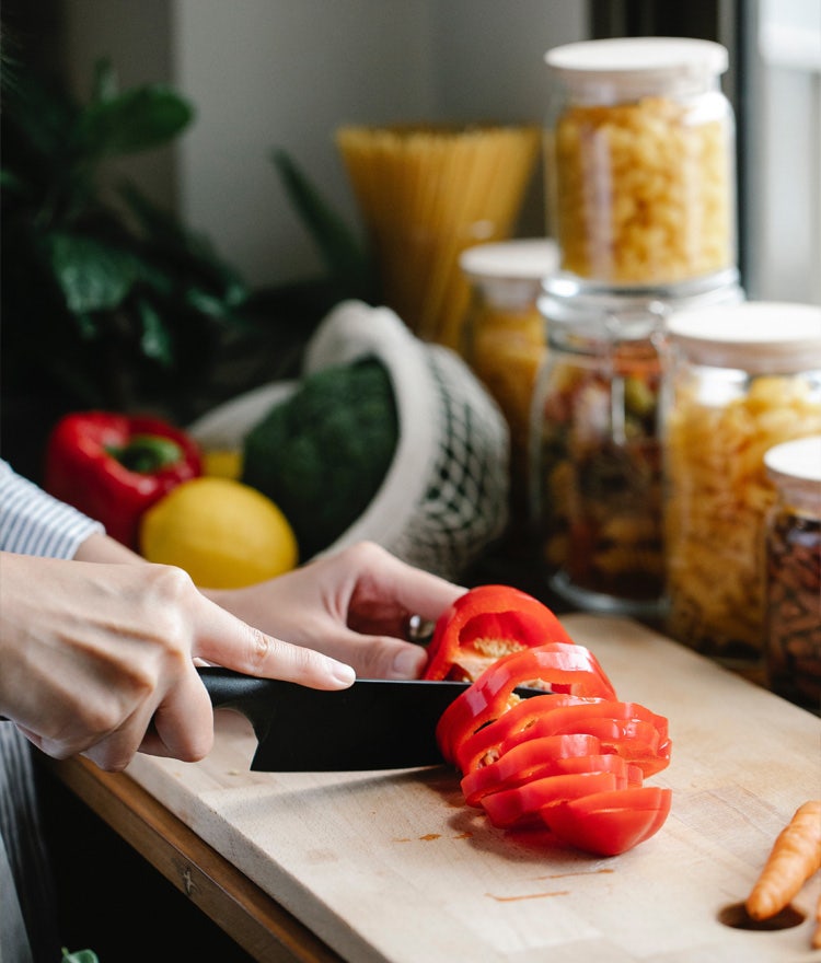 Woman's hands holding a knife and chopping red peppers