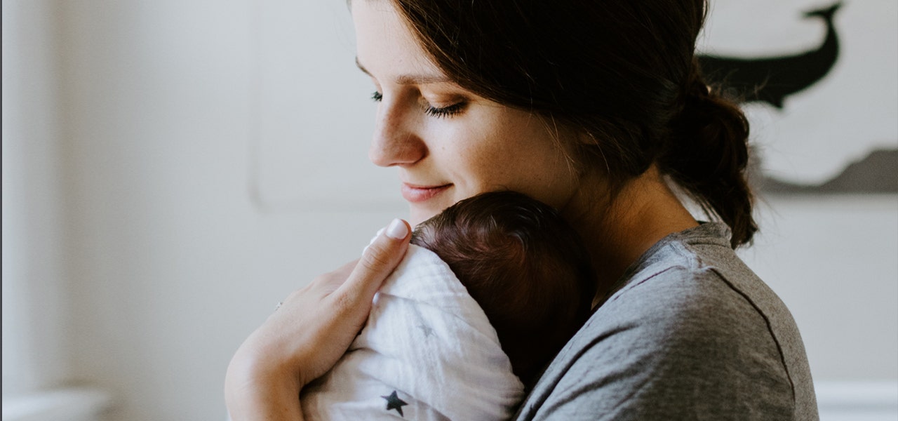 Woman cuddling a swaddled newborn, holding close to comfort them