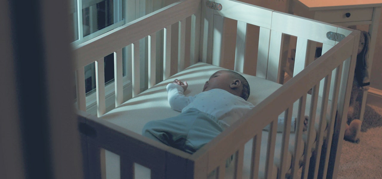 Baby lying on their back and sleeping soundly in a crib in a darkened room 