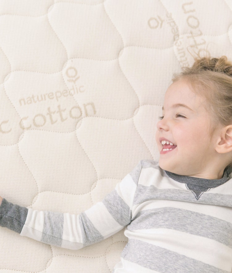 Smiling girl lying on a Naturepedic Verse Organic Kids Mattress