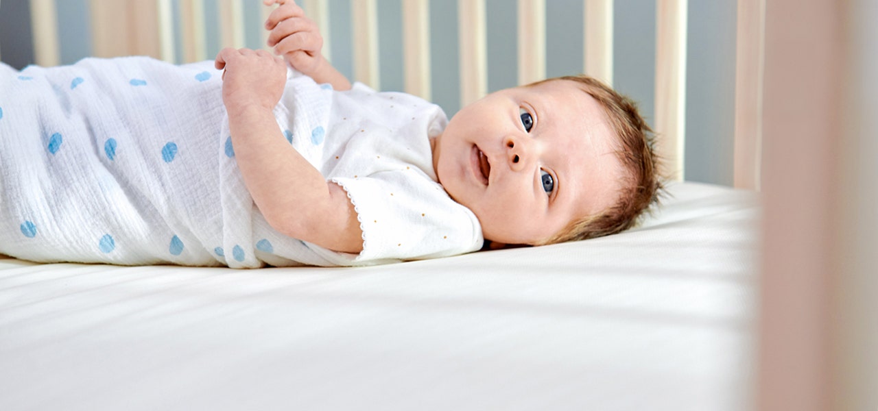 Young infant swaddled and lying awake on a firm crib mattress