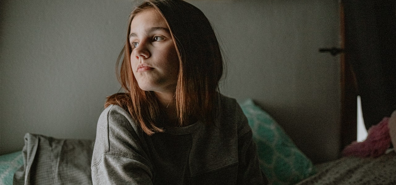 Adolescent girl sitting up in a dim bedroom and looking a little overwhelmed