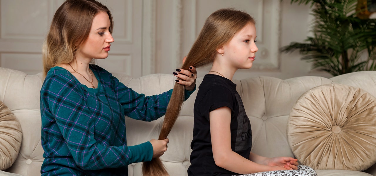 Mother sitting behind her daughter, playing with her hair