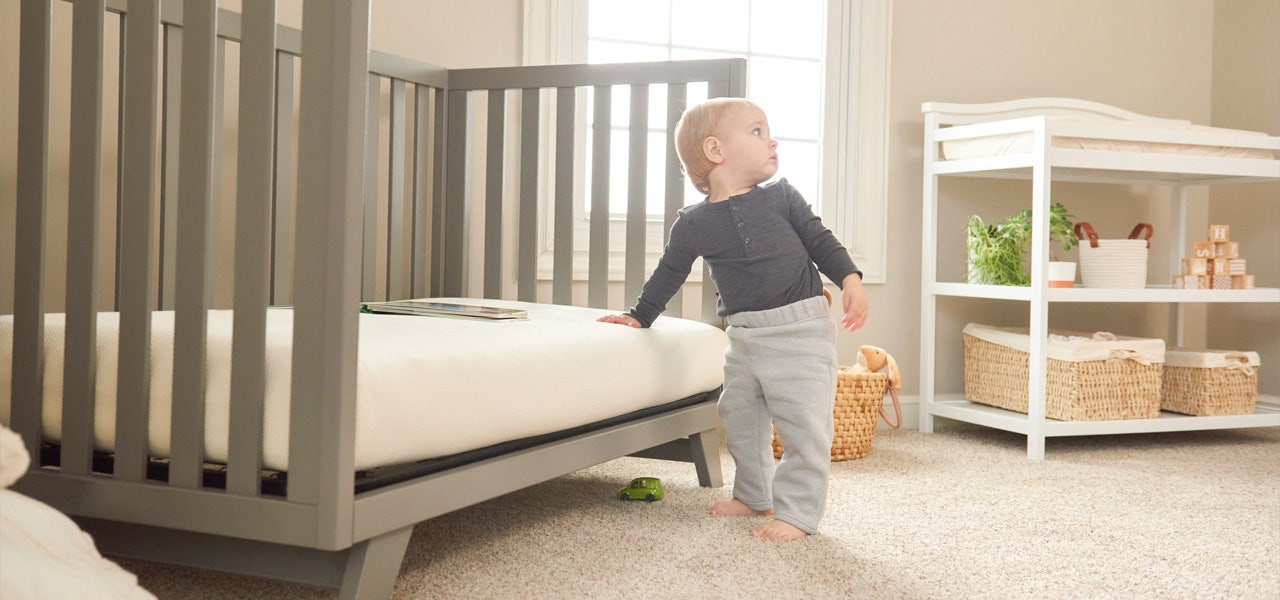 Young toddler standing near their toddler bed and holding on to the mattress