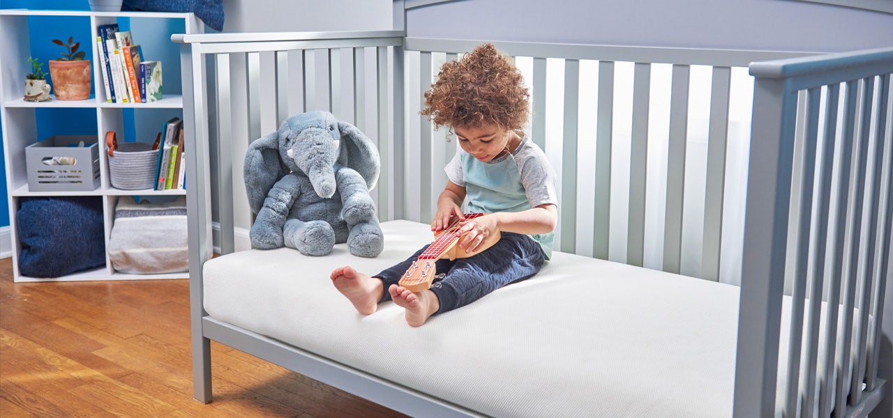 Toddler boy sitting on his big kid bed and playing with a toy guitar