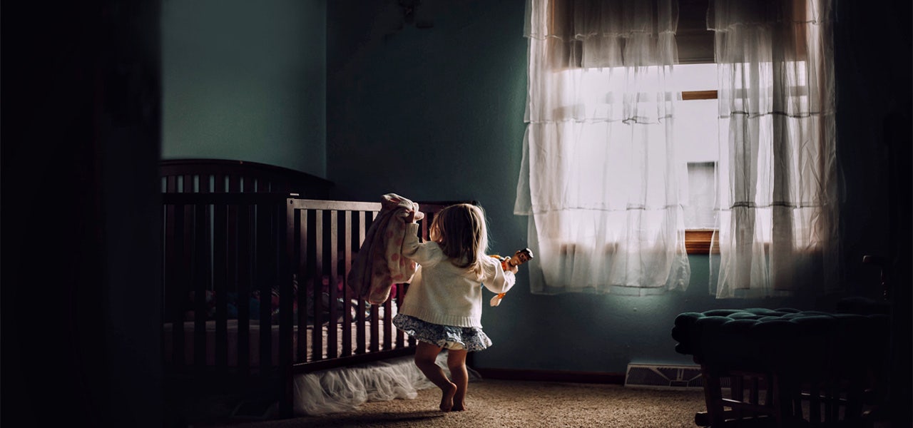 Toddler girl walling toward crib in a darkened room 