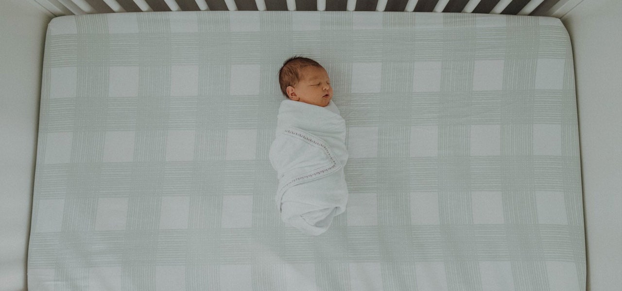Overhead image of a swaddled infant sleeping in a crib in a dim room