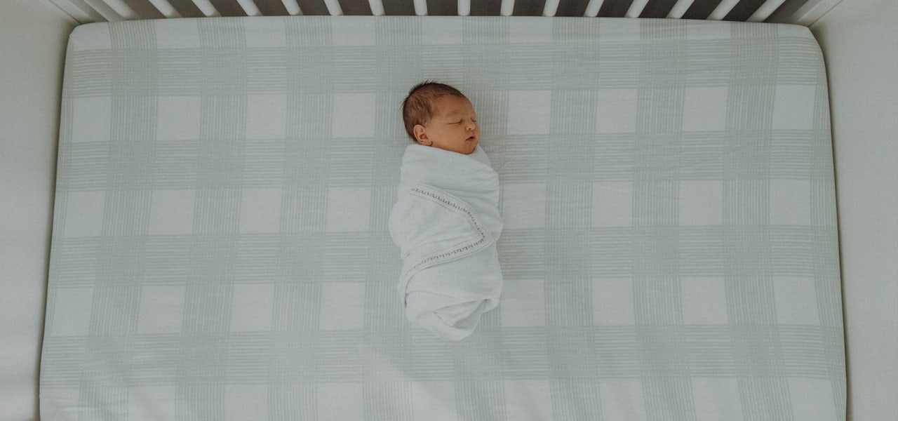 Overhead image of a swaddled infant sleeping in a crib in a dim room 