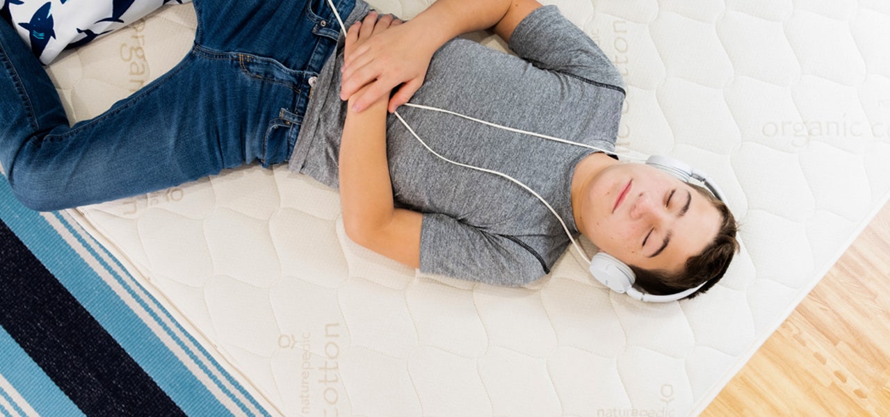 Teenaged boy wearing headphones and relaxing on a Naturepedic mattress