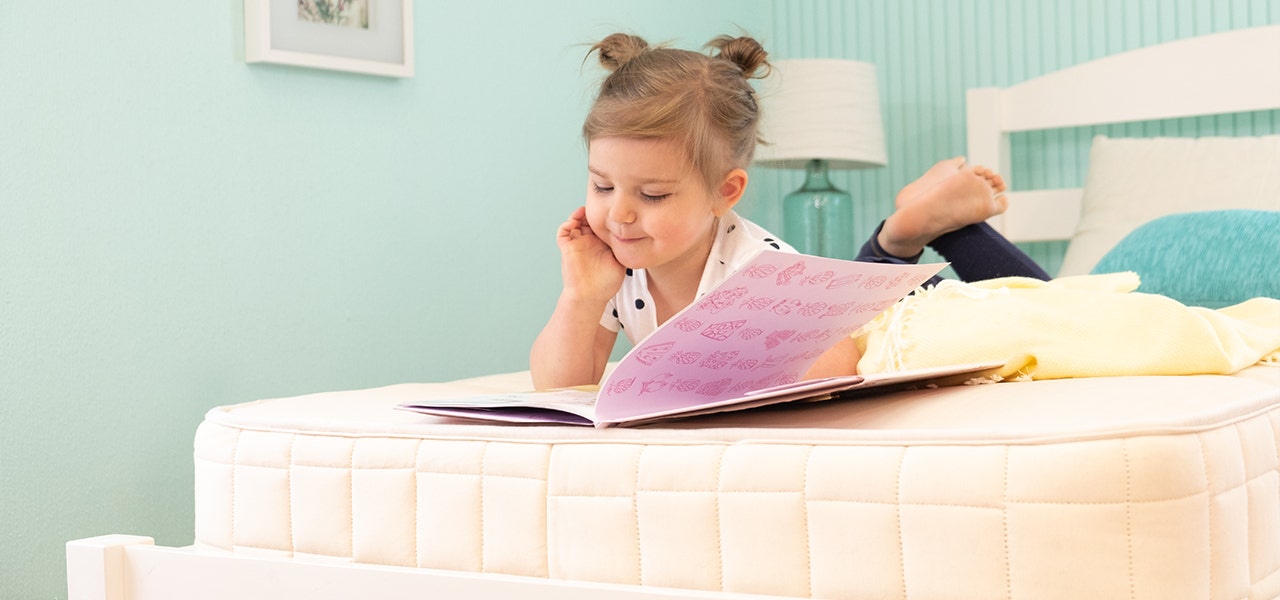 Little girl reading a book on a Naturepedic Kids Organic 2-in-1 Mattress