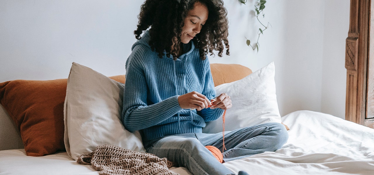Woman sitting up and knitting in bed with a body pillow for lumbar support
