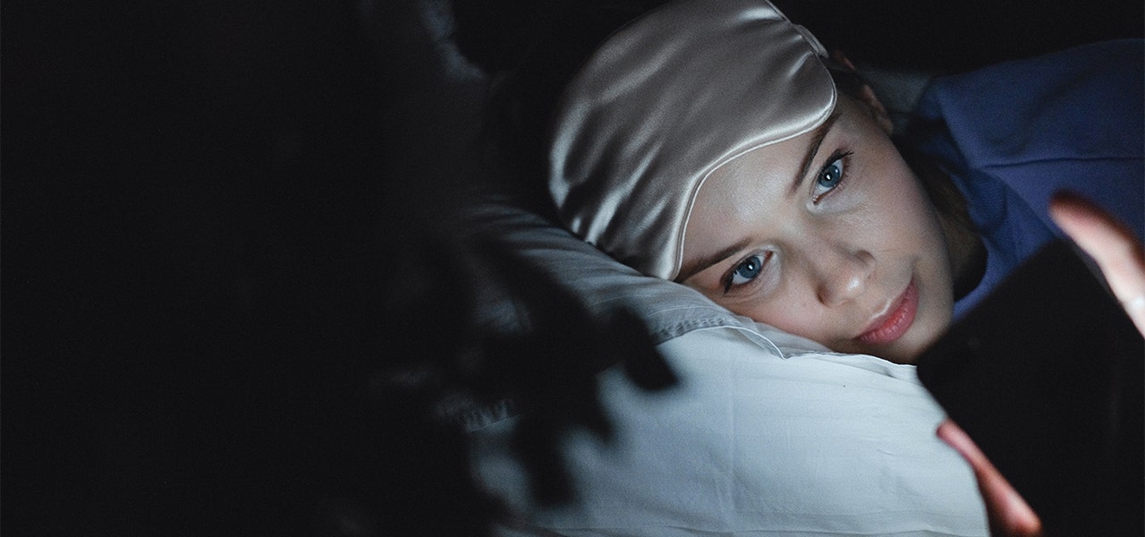 Woman lying in dark bedroom and looking at her phone