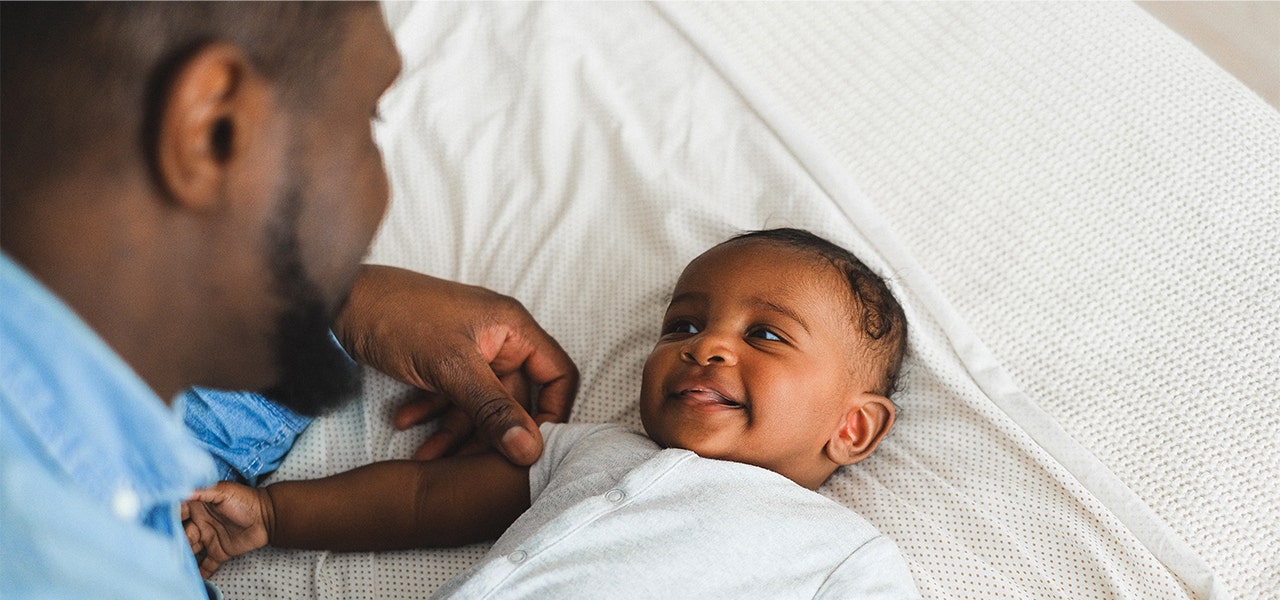 Baby lying on cool cotton bedding and smiling up at Dad