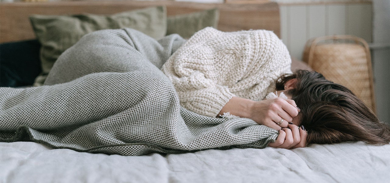 Adolescent curled up in bed and hiding their face under the blanket