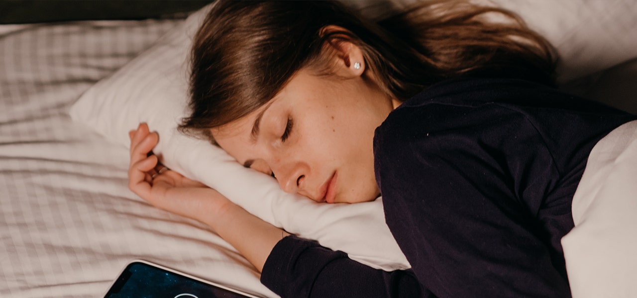 Adolescent girl asleep in bed with her phone nearby