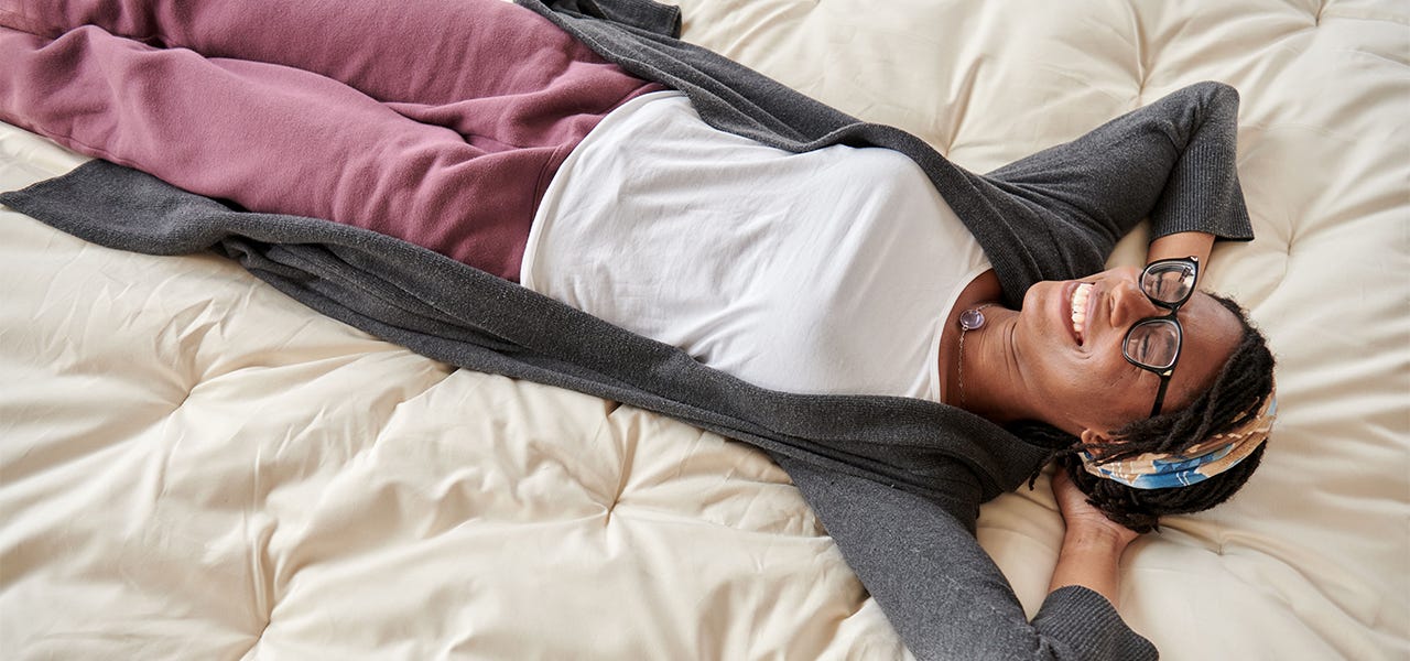 woman smiling while laying on her back on top of a naturepedic organic mattress topper