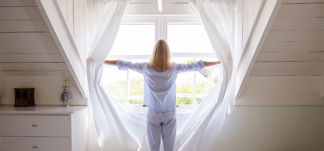 woman in pajamas opening curtains