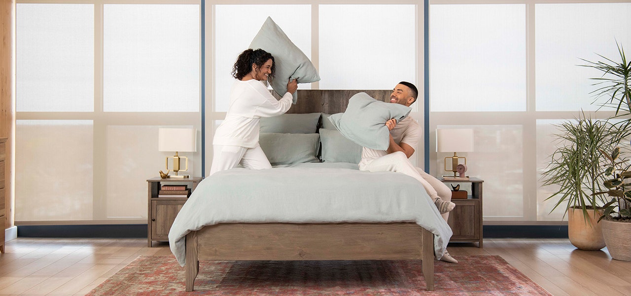 couple pillowfighting on bed with organic bedding